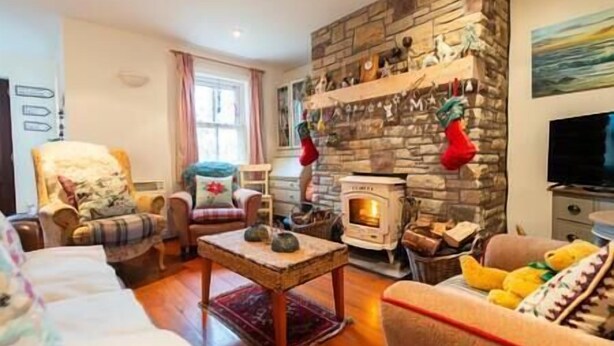 A cozy living room with a stone fireplace, a comfortable sofa, and a television. - Orchard Cottage - Dingle (Dingle)