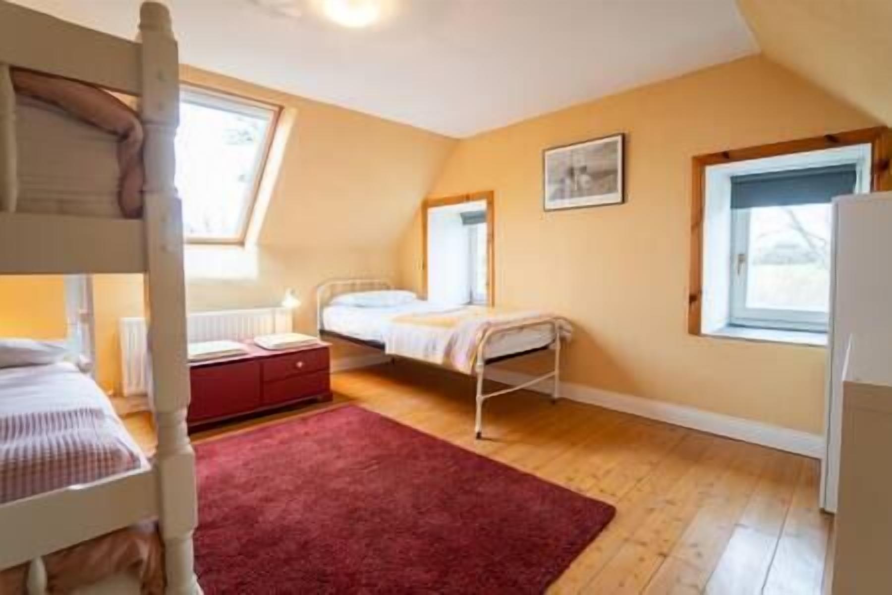 A room with a bunk bed, a single bed, a red rug, and a window with a view.