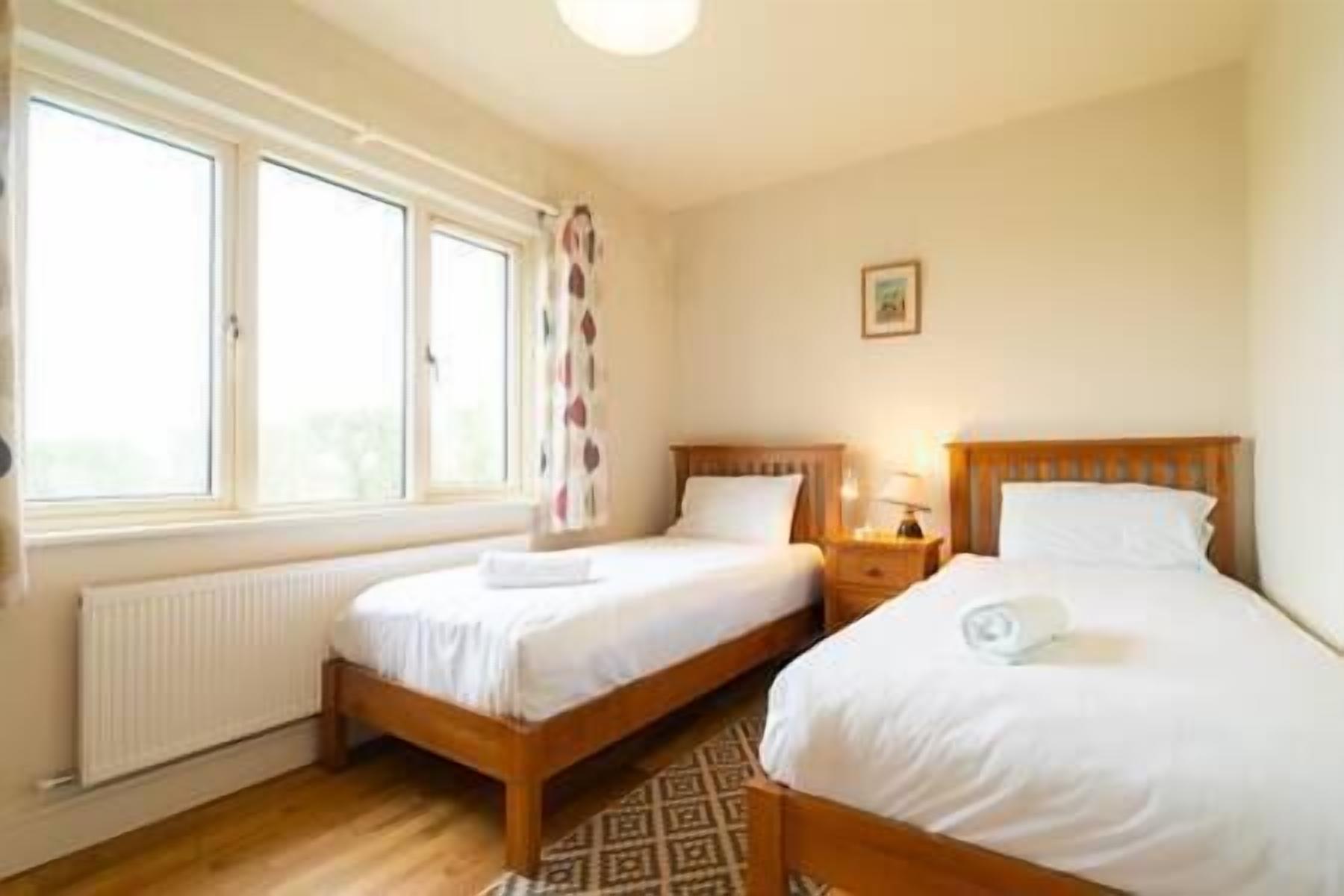 A room with two single beds, a radiator, and a window with curtains.