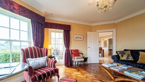 A spacious living room with a large window, a wooden coffee table with books, striped armchairs, and a sofa with decorative pillows. - Waters Edge Apartment 2 (Dingle)