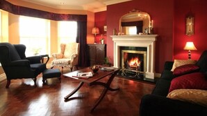 A living room with a fireplace, dark armchairs, a sofa, and a chandelier. - Waters Edge Apartment 2 (Dingle)
