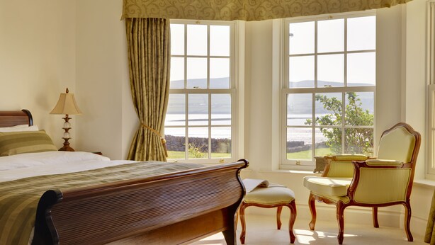 A bedroom with a large bed, a chair, a desk, and a view of the outdoors. - Waters Edge Apartment 2 (Dingle)