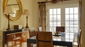 A dining area with a table, chairs, a chandelier, a mirror, and a view through large windows. - Waters Edge Apartment 2 (Dingle)