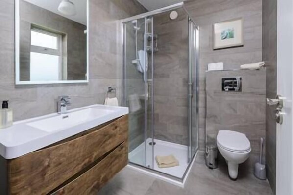 A modern bathroom with a glass shower enclosure, a wooden vanity, and a white toilet.