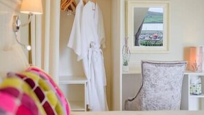 Ein Hotelzimmer mit Bett, Sessel, Bademantel an einem Kleiderhaken, Lampe und Fenster mit Landschaftsblick.