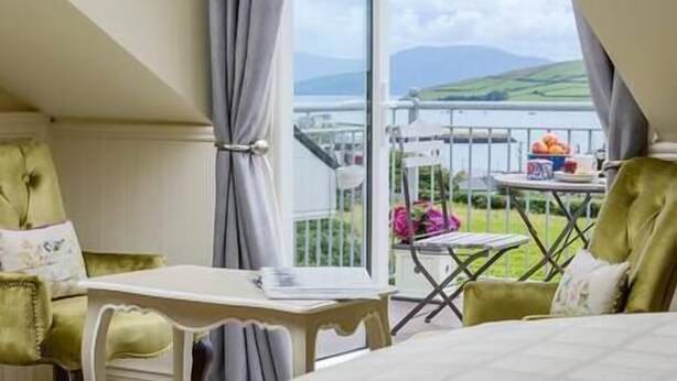 Ein Schlafzimmer mit einem Bett, einem kleinen Tisch und einem Stuhl. Ein Balkon mit Tisch und Stühlen befindet sich im Freien.