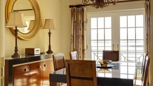 A dining area with a table, chairs, a chandelier, a mirror, and a window with curtains. - Waters Edge Apartment 1 (Dingle)
