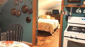 Eine gemütliche Küche mit Herd, einem Esstisch mit blumigem Tischlein und einem Bett im Hintergrund.