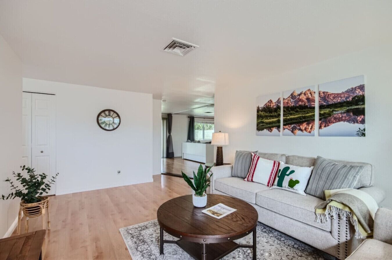 A spacious living room with a wooden floor, a round coffee table, a sofa with decorative pillows, and a large painting on the wall.