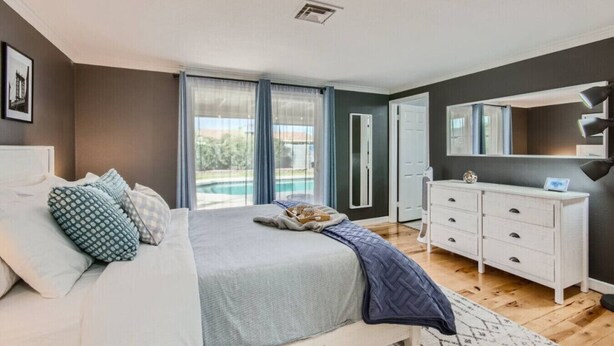 A bedroom with a bed, a dresser, a mirror, and a view of a swimming pool. - Arizona Daydream + Private Pool + EV Charger (Chandler)