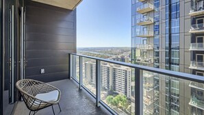 A balcony with a wicker chair, a glass railing, and a view of high-rise buildings. - 2BR + Luxury +Views +Rooftop pool in Austin (Austin)