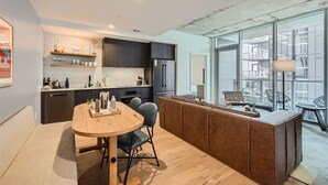 A modern kitchen with dark cabinets, a wooden dining table, and a large window overlooking a cityscape. - 2BR + Luxury +Views +Rooftop pool in Austin (Austin)