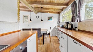 A kitchen with wooden beams, a dining table, chairs, a coffee maker, and a window with curtains. - 3 bedroom nice home in Melby (Melby)