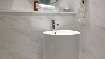 A bathroom with a large white sink, a round mirror, a towel rack, and a hairdryer on the wall.