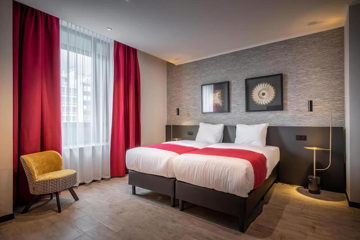 A modern hotel room with a large bed, red curtains, and two wall art pieces.