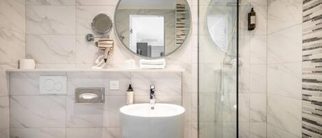 Un bagno moderno con un grande specchio rotondo, un lavandino e una cabina doccia in vetro.