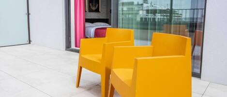 Une chambre moderne avec un lit, une porte en verre et un balcon agrémenté de chaises jaunes.