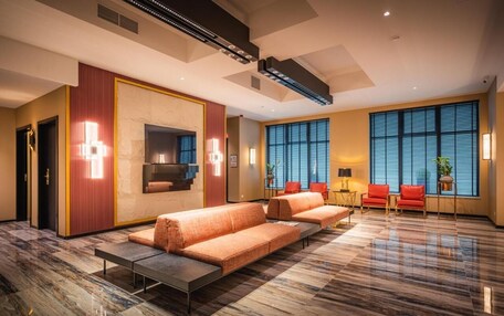 A modern hotel lobby with a marble floor, a sofa set, a fireplace, and large windows with blinds.