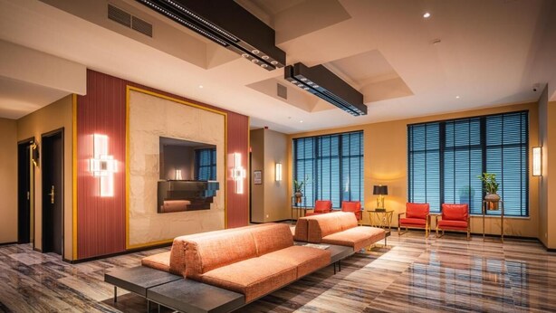 A modern hotel lobby with a marble floor, a sofa set, a fireplace, and large windows with blinds. - Hotel Jamingo (Antwerp)