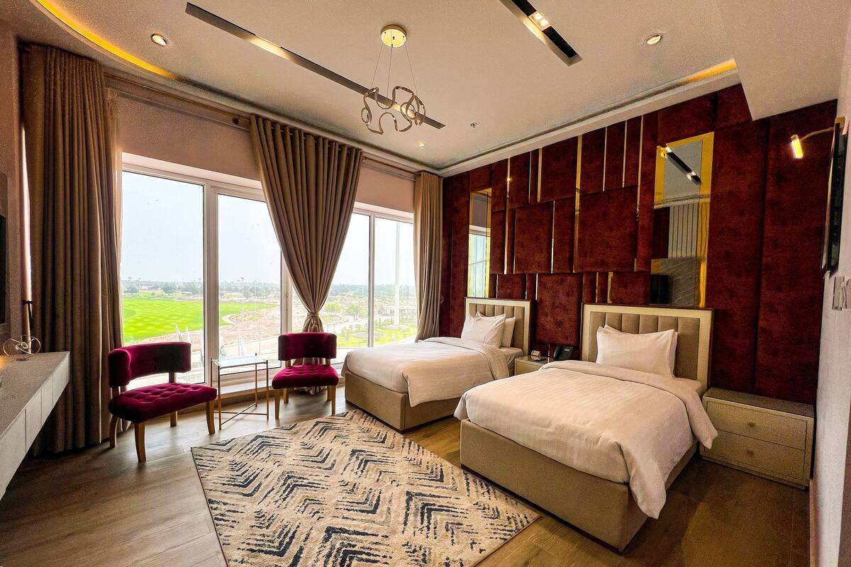 Habitación de hotel con dos camas, un ventanal con vistas, una silla roja y una alfombra estampada.