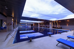 An indoor swimming pool with a modern design, including a skylight and lounge area with blue benches.