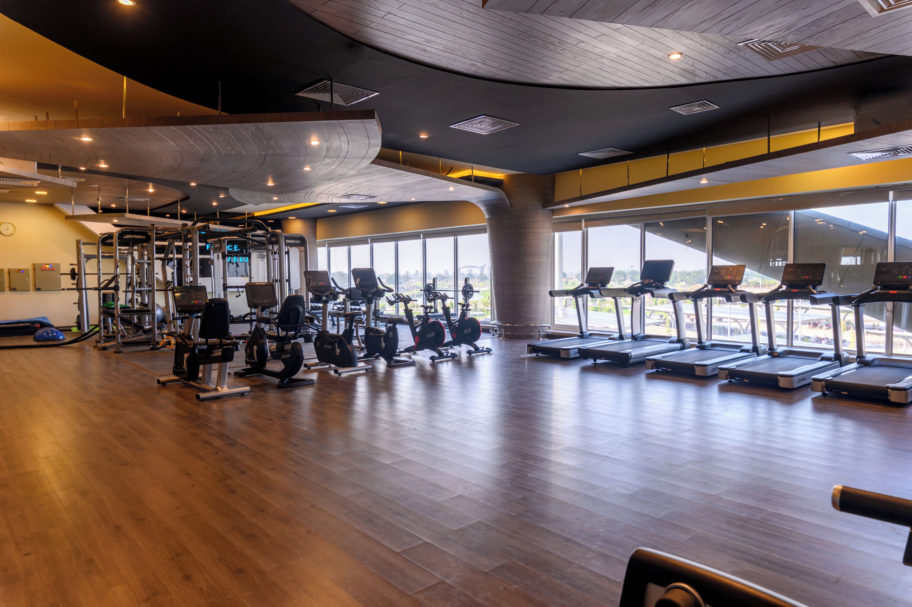 A gym with cardio equipment, weight machines, and a large window offering a view of the outdoors.