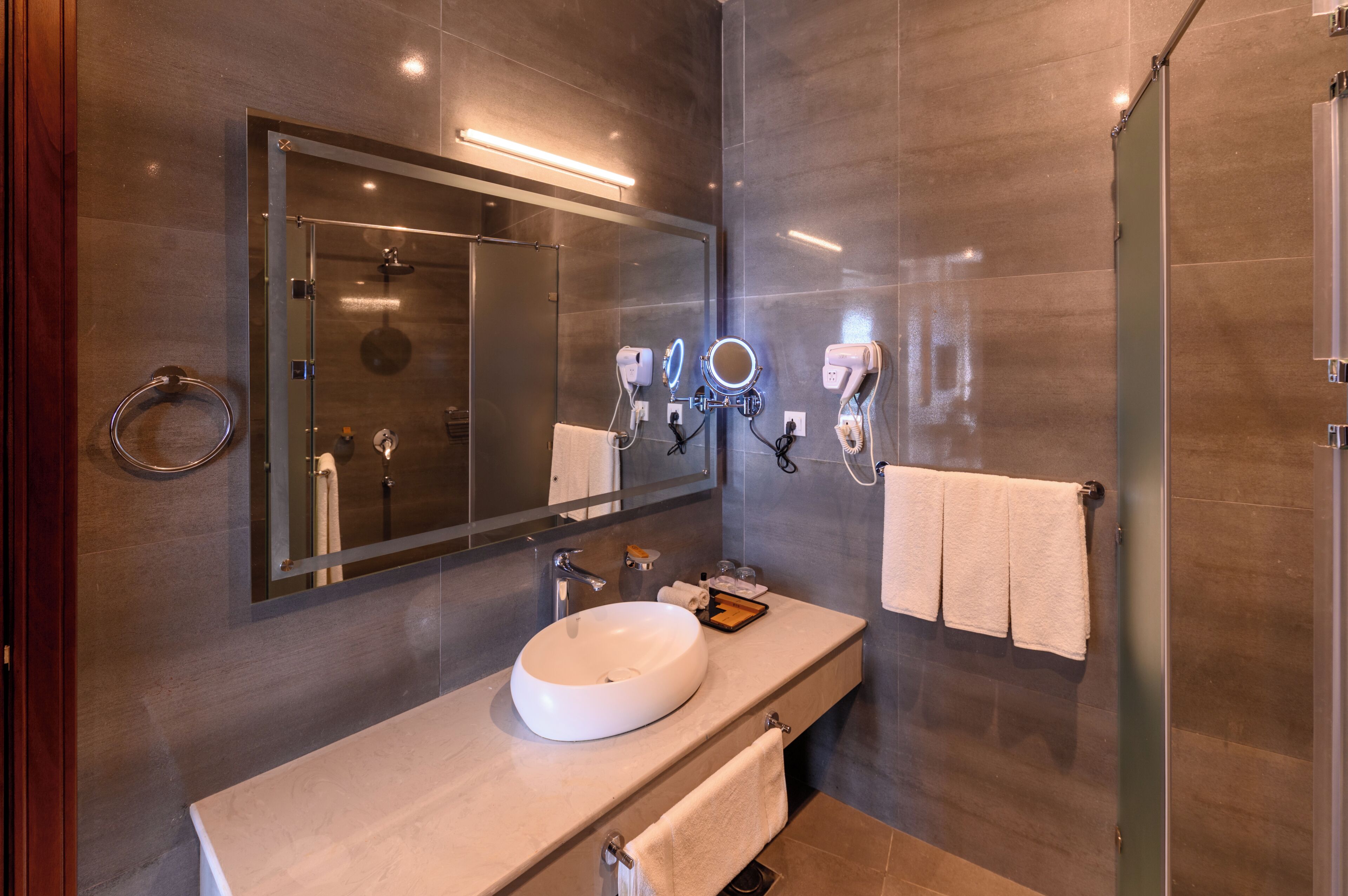 A modern bathroom with a large mirror, a round sink, and a glass shower enclosure.