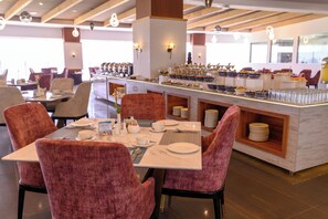 A hotel dining area with tables set for breakfast, including bowls of cereal and fruits.