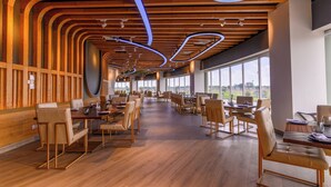 A spacious restaurant with wooden paneling, modern lighting, and large windows offering a view. - Rumanza by Pearl Continental (Multan)