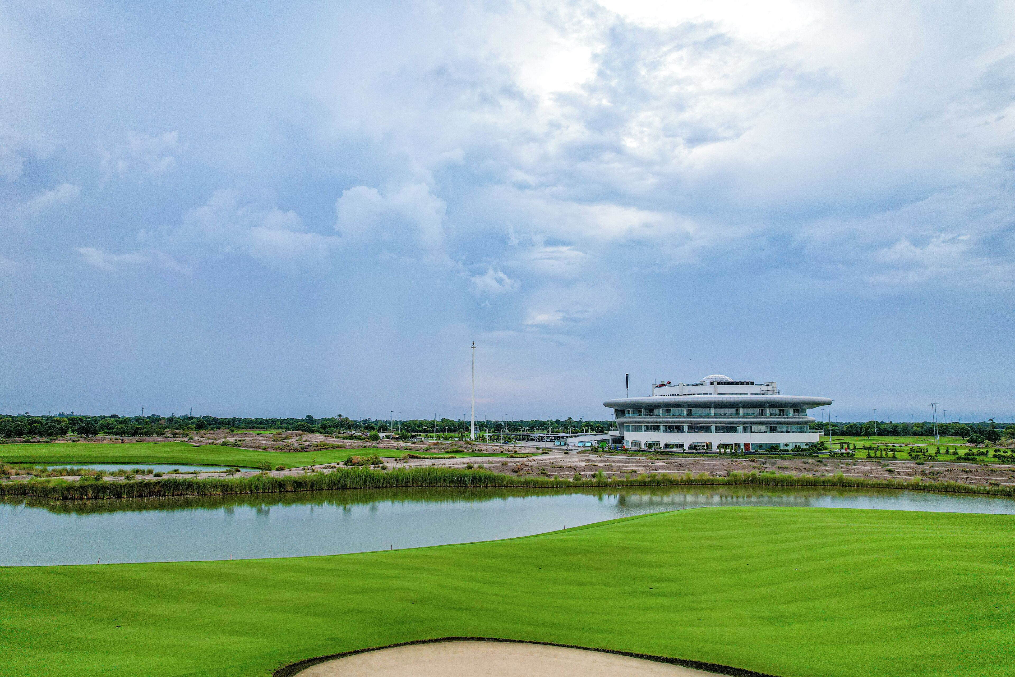 Ein Golfplatz mit einem modernen Gebäude, einem Teich und blauem Himmel.