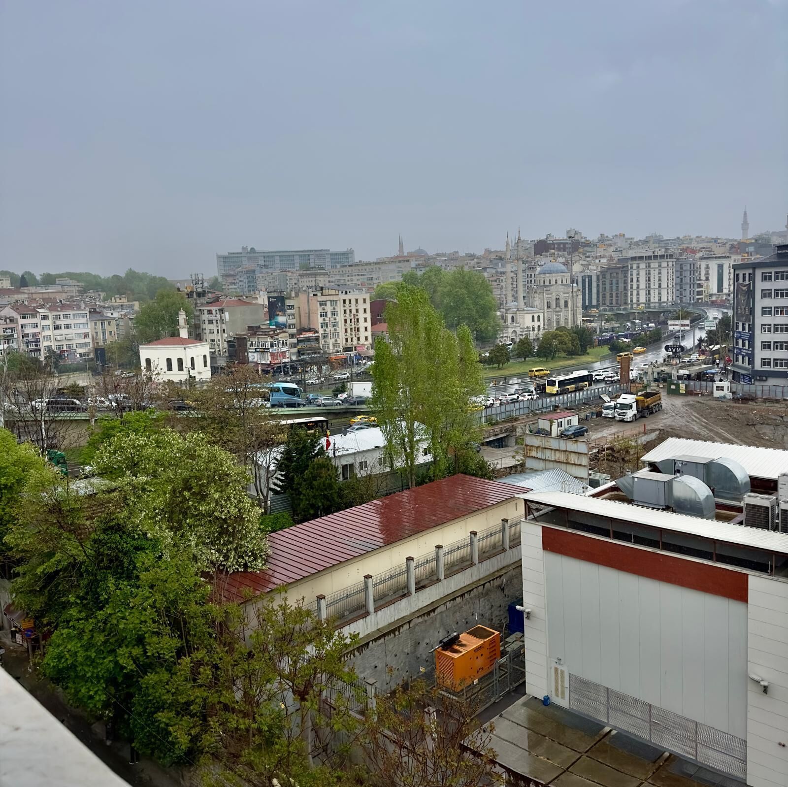 Eine Stadtansicht mit verschiedenen Gebäuden, einer markanten Moschee und einer belebten Straße mit Fahrzeugen.