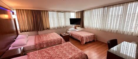 Une chambre d’hôtel avec deux lits, une télévision, un bureau et de grandes fenêtres avec des rideaux.