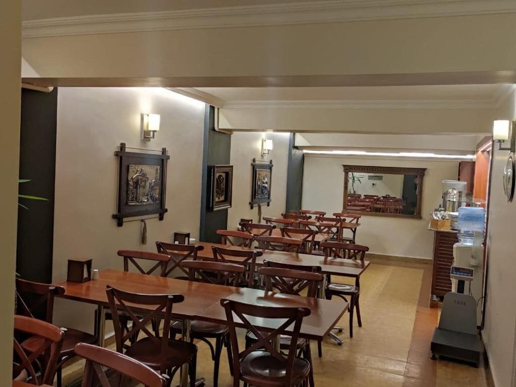 A dining area with multiple wooden tables and chairs, framed artwork on the walls, and a water dispenser in the corner.