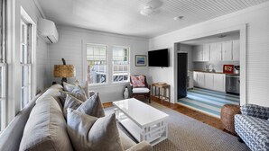A modern living room with a sofa, a coffee table, and a TV. There is a kitchen visible through an open doorway. - Charming Second Row Beach House - 1st Floor Only, 2 Screened Porches, Grill (Pawleys Island)