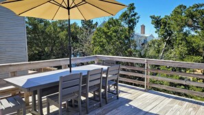 A wooden deck with a table and chairs, a large umbrella, and a railing. - Charming Second Row Beach House - 1st Floor Only, 2 Screened Porches, Grill (Pawleys Island)