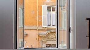 A view through a window of a building with a white door and a window with white shutters. - 4bnb - Lungaretta Jacuzzi Apartment (Rome)