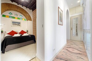 A hotel room with a bed, red pillows, a framed picture, a tiled floor, and a doorway leading to another room. - 4bnb - Lungaretta Jacuzzi Apartment (Rome)