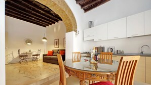 A dining area with a glass table, wooden chairs, and a red cushion. There is a kitchen with white cabinets and a sink. - 4bnb - Lungaretta Jacuzzi Apartment (Rome)