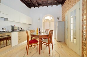 A modern kitchen with white cabinets, a dining table with chairs, and a refrigerator. - 4bnb - Lungaretta Jacuzzi Apartment (Rome)