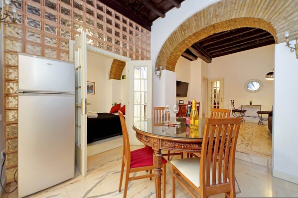 A dining area with a round table, chairs, and a refrigerator in the background. - 4bnb - Lungaretta Jacuzzi Apartment (Rome)