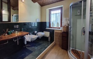 Ein modernes Badezimmer mit einem großen Spiegel, einem Holzwaschtisch, einem Bidet, einer Duschkabine aus Glas und einem Fenster mit Vorhängen.