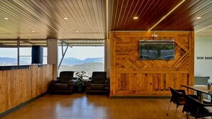 A spacious room with wooden walls and a large window offering a view of the mountains. There is a wooden wall with a mounted television and a sign that reads "WASH BASIN". - The Royal Heaven by Joy Suites (Wai)