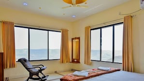 A hotel room with a bed, a rocking chair, a large window with curtains, and a ceiling fan. - The Royal Heaven by Joy Suites (Wai)