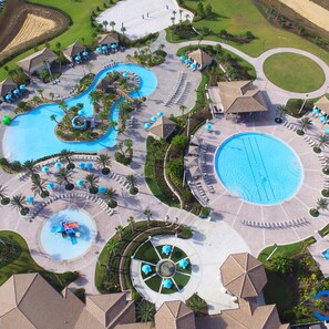 Luchtbeeld van een resort met meerdere zwembaden, ligbedden en palmbomen.