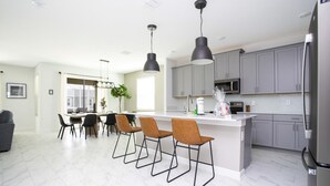 A modern kitchen with grey cabinets, a stainless steel refrigerator, and a dining area with bar stools. - Amazing Resort Private Pool Chg102 (Davenport)