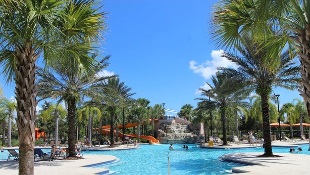 A pool area with palm trees, a water slide, and a clear blue sky. - Bright Elegant Home at Solterra Resort Sol103 (Davenport)