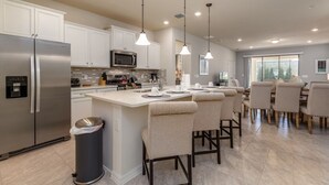 A modern kitchen with stainless steel appliances, a central island with bar stools, and pendant lighting. - Bright Elegant Home at Solterra Resort Sol103 (Davenport)