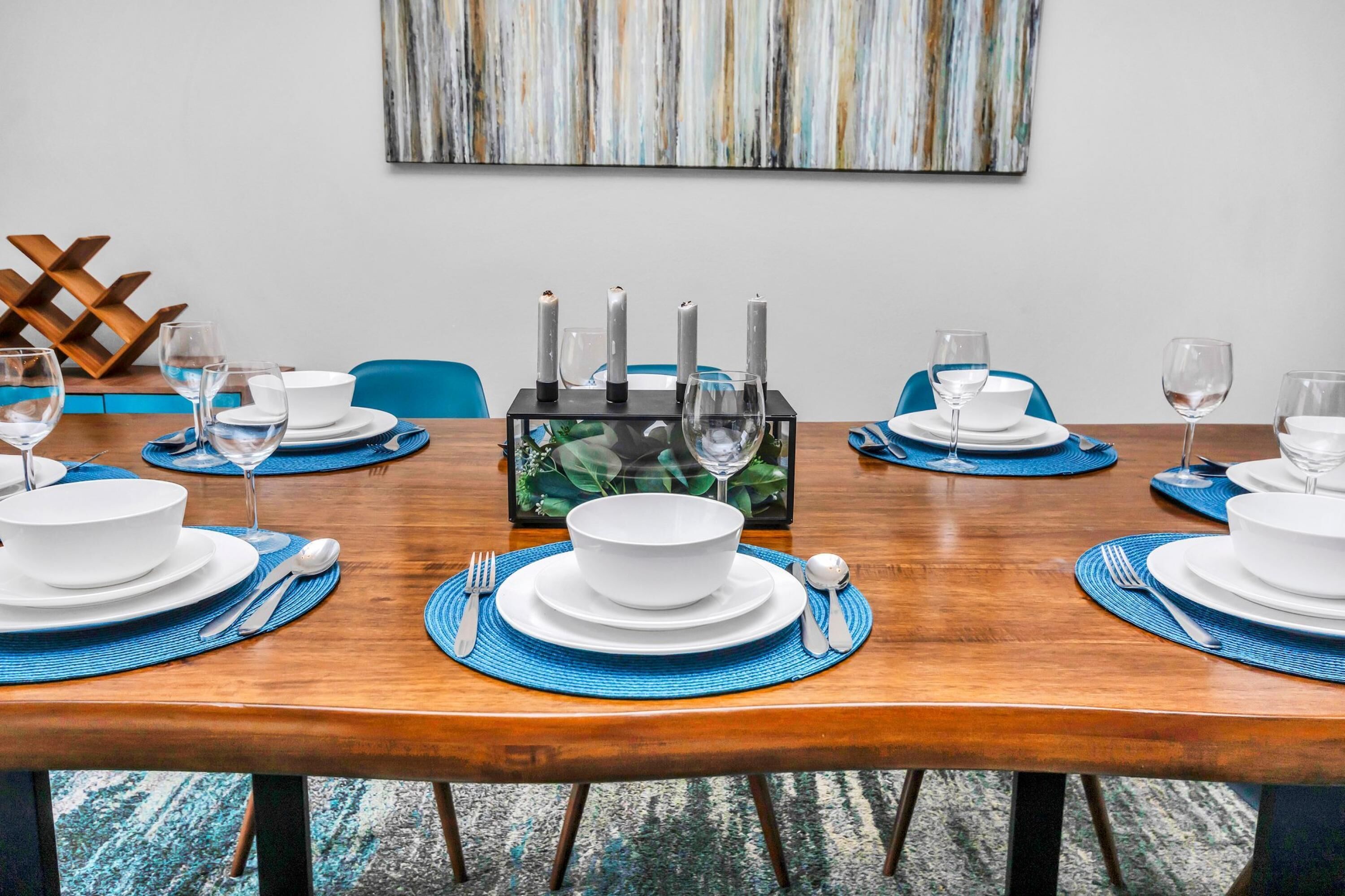 A dining table set with white plates, bowls, and cutlery, blue placemats, and candles.