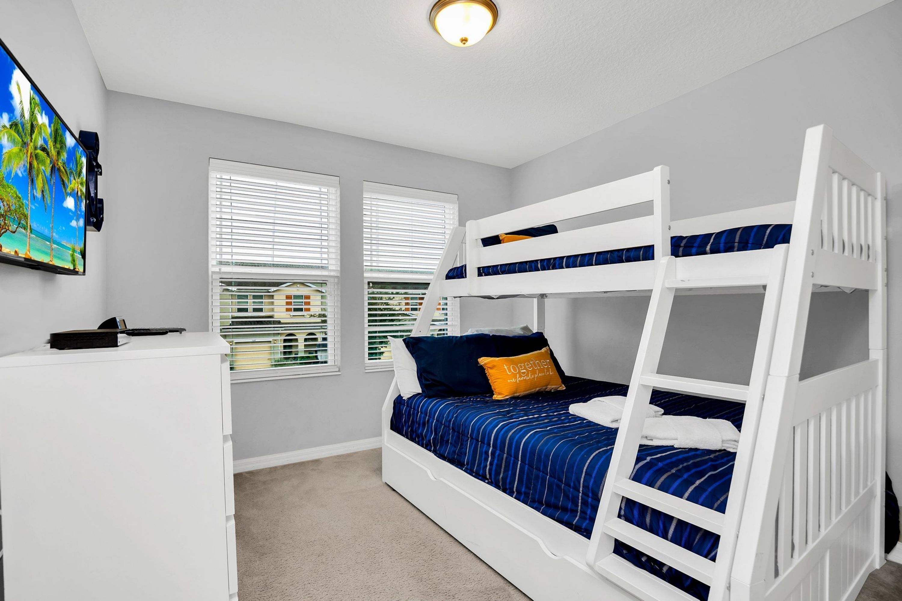 A bunk bed room with a desk, two windows, and a ceiling light.