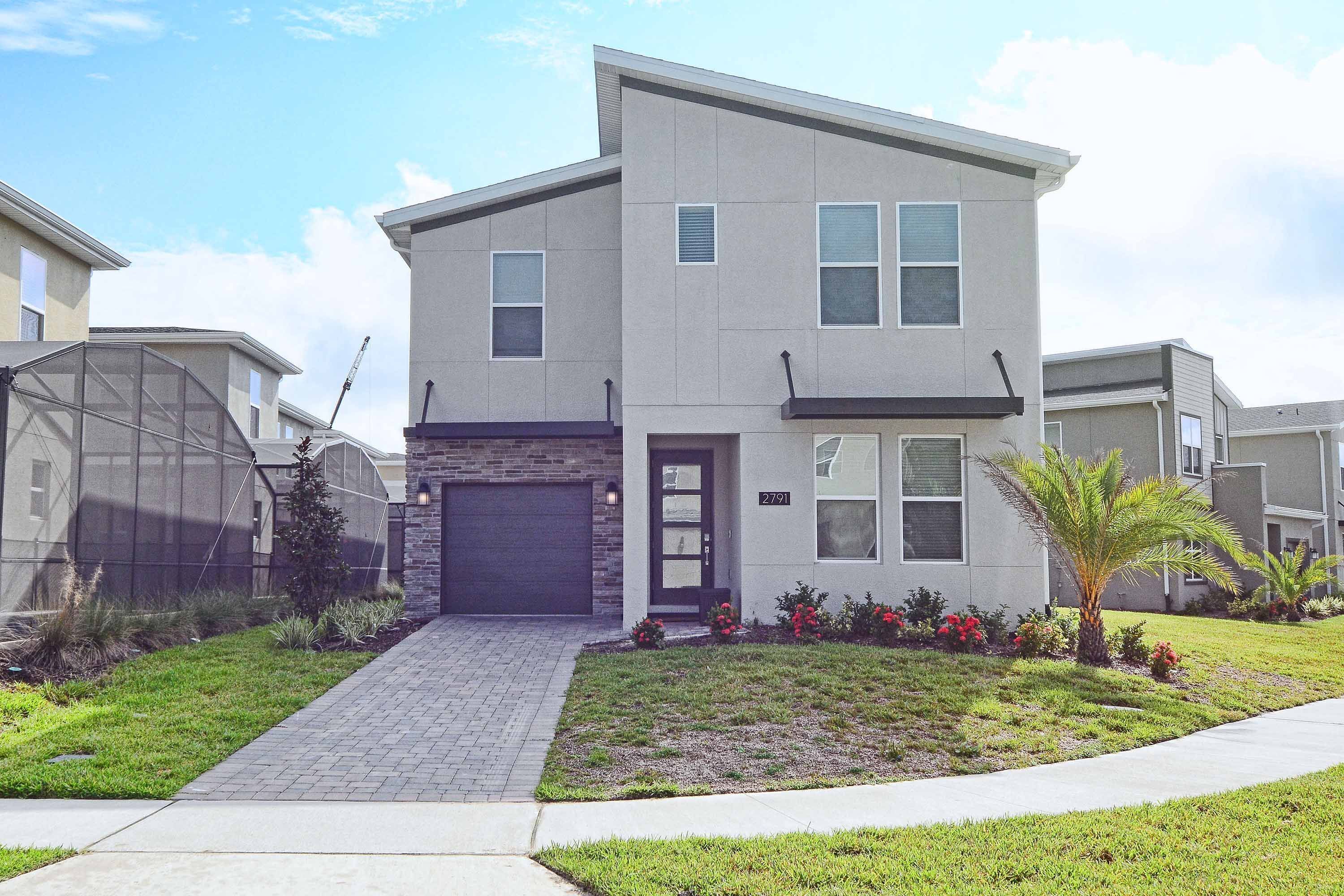 A modern two-story residential building with a garage, a well-maintained lawn, and a small palm tree.